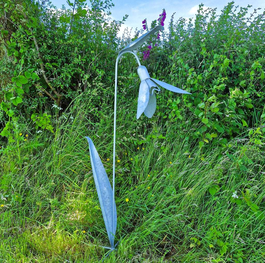 Metallic sculpture of a snowdrop flower in a natural setting with greenery