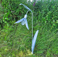 Metal sculpture of a flower in a natural setting with greenery