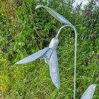 Metallic sculpture of a flower in a natural setting with greenery