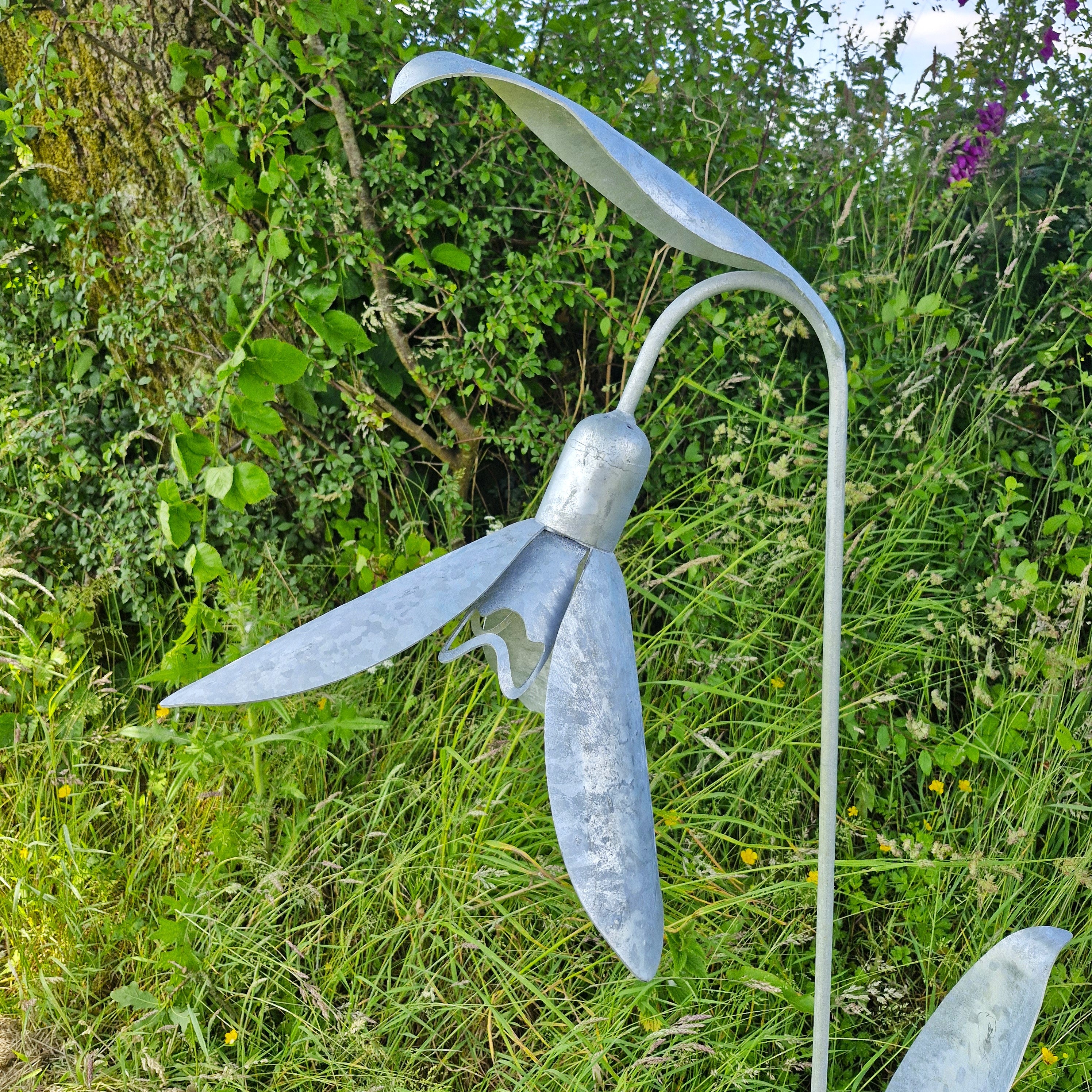 Metallic sculpture of a flower in a natural setting with greenery